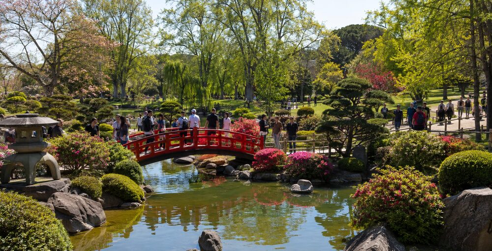 Jardín Japonés de Palermo con numerosos visitantes recorriendo el puente rojo, el estanque y sus jardines de colores vivos.