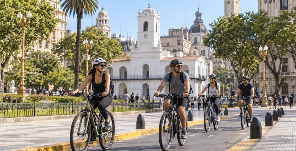 Ciclistas recorren una calle junto a la Plaza de Mayo, con el Cabildo de fondo, en una imagen ilustrativa sobre la bicicleteada por el Casco Histórico