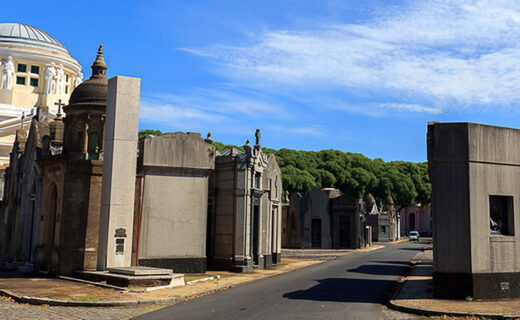 Calle interna del Cementerio de la Chacarita, rodeada de bóvedas y panteones bajo un cielo azul.