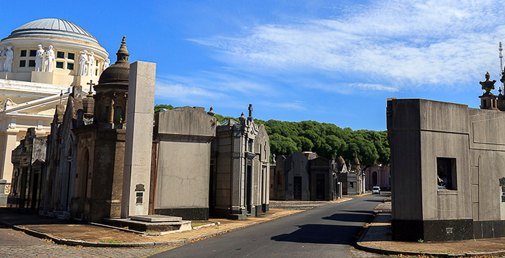 Calle interna del Cementerio de la Chacarita, rodeada de bóvedas y panteones bajo un cielo azul.