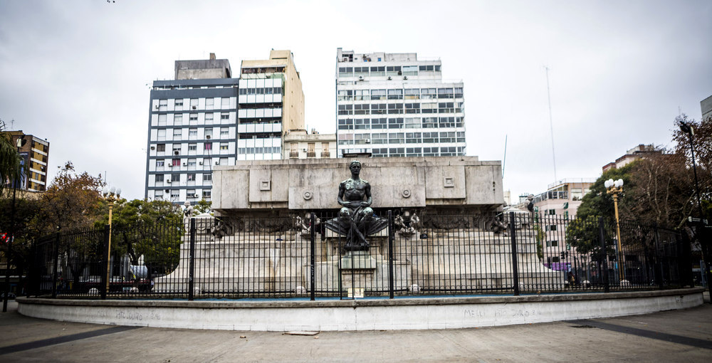 Mausoleo de Bernardino Rivadavia visto de frente en Plaza Miserere, con su escultura de bronce y los edificios de Once al fondo.