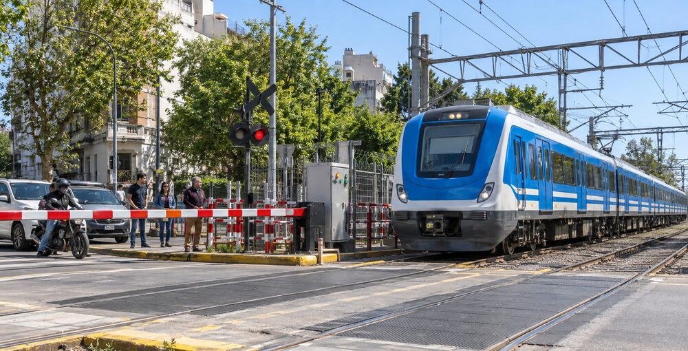 Tren Sarmiento atravesando un paso a nivel con la barrera baja y un nuevo sistema de monitoreo ferroviario.