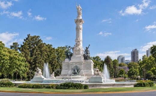 Monumento de los Españoles con sus esculturas y fuentes, rodeado por la vegetación de Palermo bajo un cielo azul.