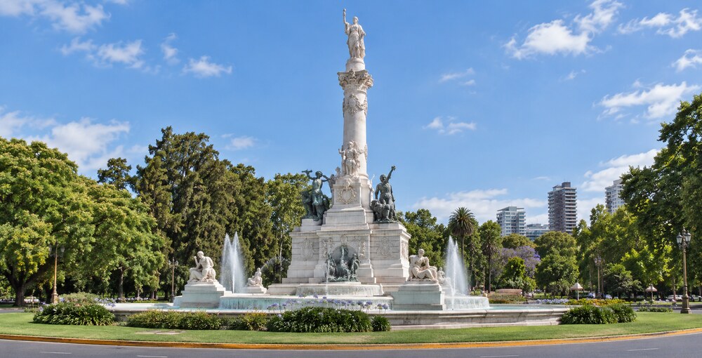 Monumento de los Españoles con sus esculturas y fuentes, rodeado por la vegetación de Palermo bajo un cielo azul.