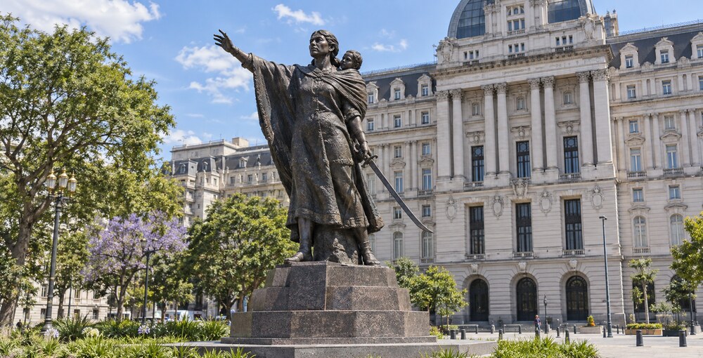 Monumento a Juana Azurduy en la Plaza del Correo, con el Palacio Libertad y la vegetación del Bajo porteño de fondo.