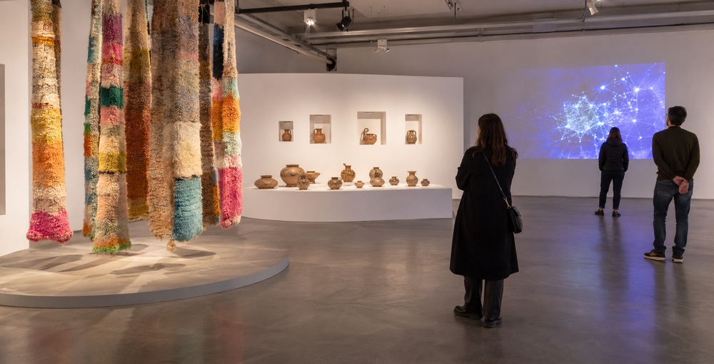 Visitantes recorren una sala de arte contemporáneo con instalaciones textiles, piezas de cerámica y una proyección tecnológica vinculada a las muestras del Museo Moderno y el Centro Cultural Recoleta.