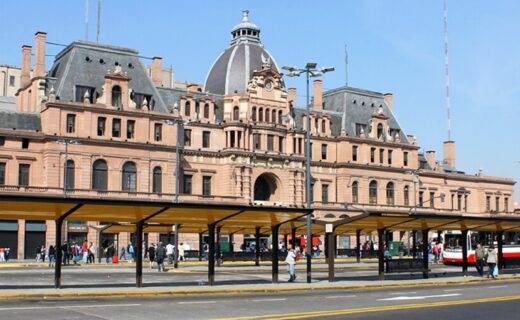 Frente histórico de la estación Plaza Constitución con su cúpula central, mansardas y movimiento del transporte público porteño.