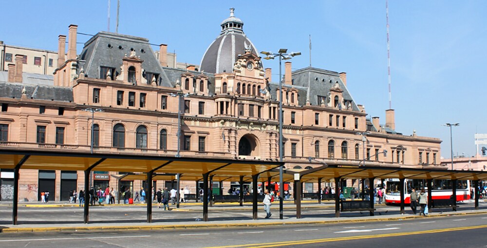 Frente histórico de la estación Plaza Constitución con su cúpula central, mansardas y movimiento del transporte público porteño.