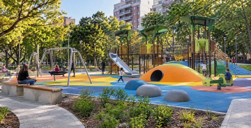 Patio de juegos renovado de Plaza Almagro con mangrullos, hamacas, suelo de colores y familias disfrutando del espacio verde.