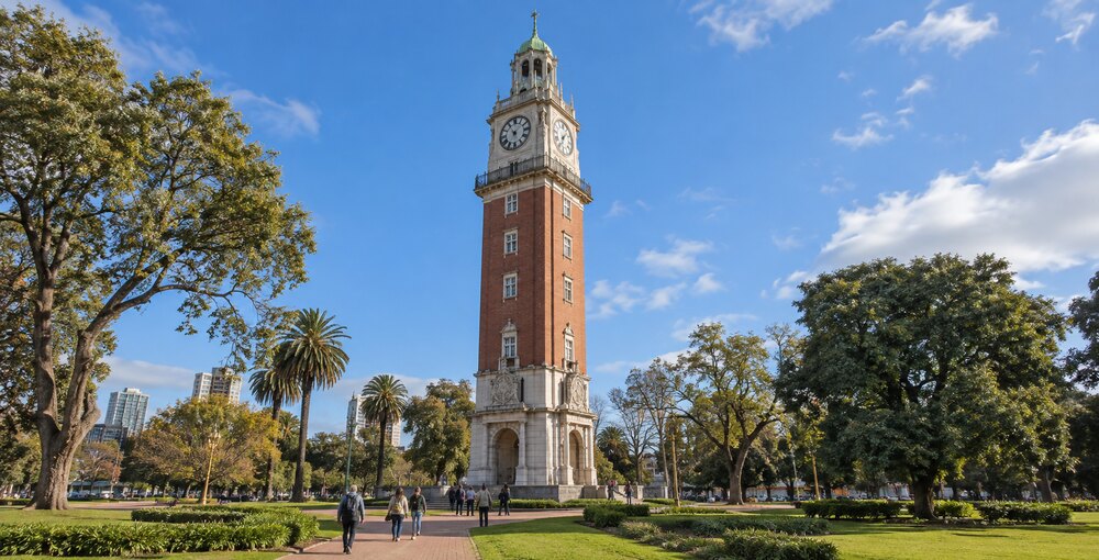 Torre Monumental rodeada de árboles y visitantes en el barrio porteño de Retiro durante una jornada soleada.