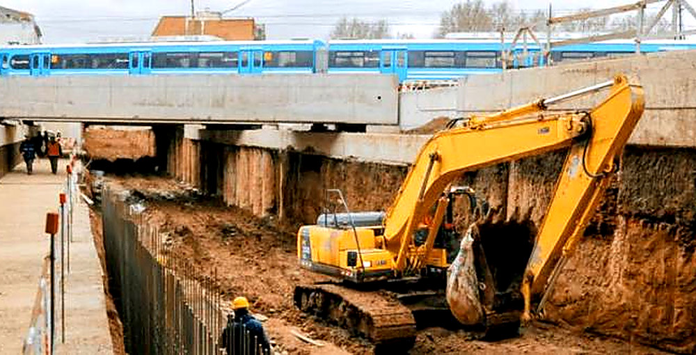 Obras del paso bajo nivel Irigoyen en Villa Luro, con una excavadora y un tren Sarmiento, donde los vecinos podrán elegir el nombre del túnel.